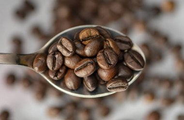 Koyu dokulu arka planda kavrulmuş kahve çekirdekleri ile dolu bir kaşık. Kavram: kahve çekirdeği ihracatı ve ithalatı, kahve tüketimi.