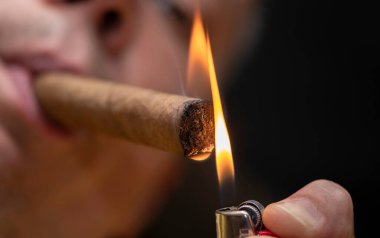 Bir adam koyu arka plandaki çakmağından puro yakar, yakın plan, seçici odak.