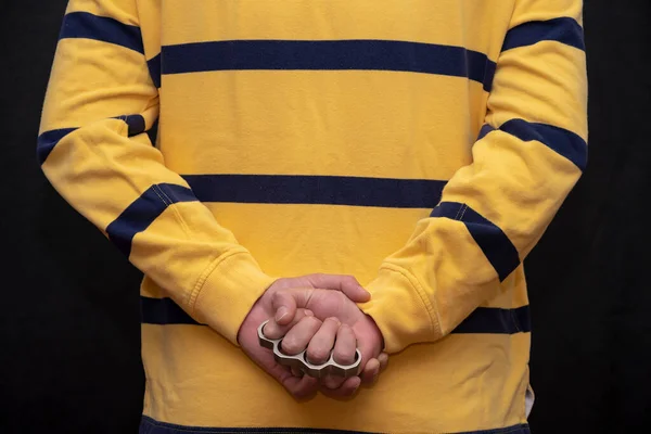 黄色のセーターの男は 戦いの準備をしながら 背中の後ろに金属真鍮ナックルを保持しています コンセプト ストリートギャング 市内の犯罪 — ストック写真