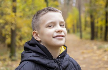 Sonbahar sarısı bir ormanın arka planında ceketli gülümseyen 10 yaşındaki bir çocuğun portresi. Konsept: sonbahar tatili, yakında okula gitmek, ormanda yürümek, gezmek ve doğadaki çocukları eğlendirmek..