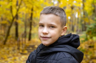Sonbahar sarısı bir ormanın arka planında ceketli gülümseyen 10 yaşındaki bir çocuğun portresi. Konsept: sonbahar tatili, yakında okula gitmek, ormanda yürümek, gezmek ve doğadaki çocukları eğlendirmek..