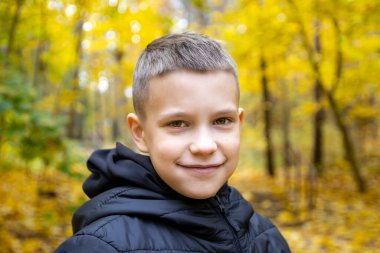 Sonbahar sarısı bir ormanın arka planında ceketli gülümseyen 10 yaşındaki bir çocuğun portresi. Konsept: sonbahar tatili, yakında okula gitmek, ormanda yürümek, gezmek ve doğadaki çocukları eğlendirmek..