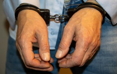 Hafif arka planda kelepçeli bir adam. Kavram: tutuklu bir suçlu, karakolda kaçak bir göçmen, sınır ihlali, rüşvet alan ve yolsuzluğa bulaşmış bir memur, tutuklu.