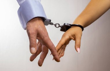 Kelepçeli iki elin yakın çekimi, bir erkek ve bir kadın. Kavram: evli bir çiftin birbirlerine bağlılığı. Sevgi dolu bir çift. Aşk, ilişkiler, romantizm, seks, suç, ceza, hapis.
