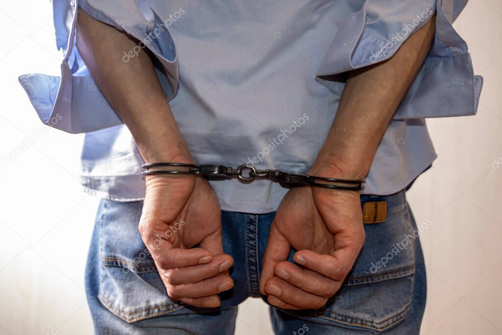 A man handcuffed on a light background. Concept: a detained criminal, an illegal migrant in a police station, a border violator, a bribe taker and a corrupt official, arrest.