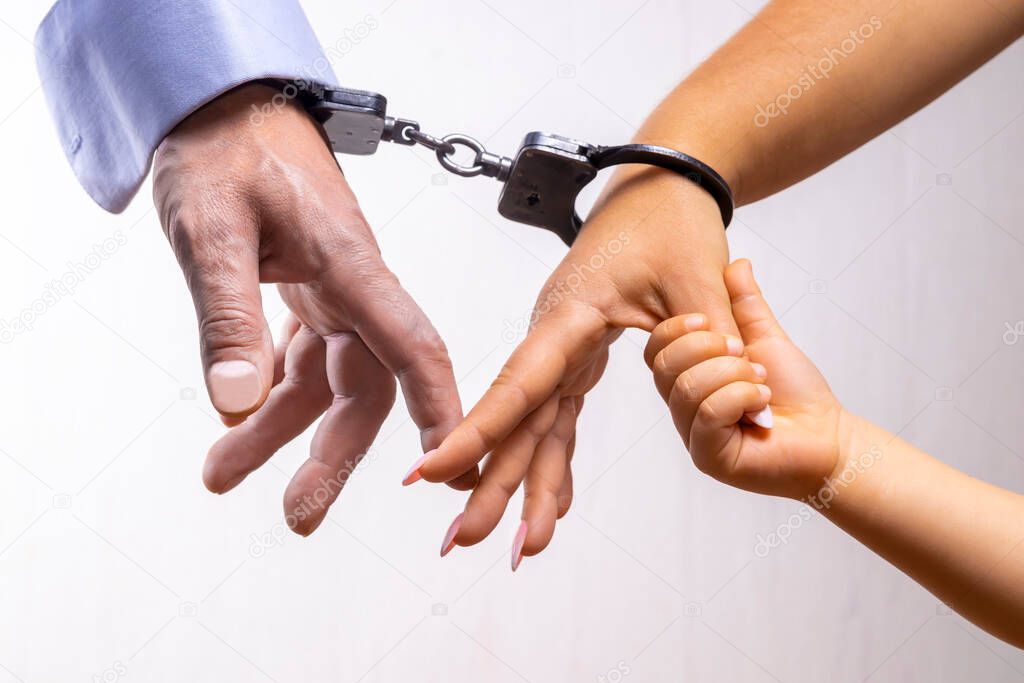 Male and female hands are handcuffed. The child's hand is holding on to the mother's finger, light background, selective focus, close-up. Concept: family ties of love, childhood affection, kinship.