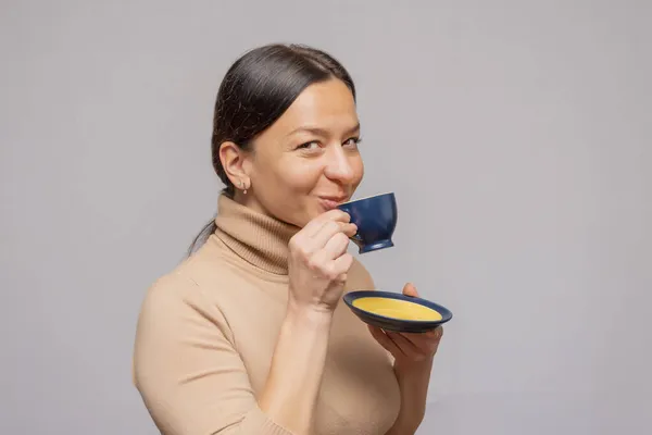 工作室里一个漂亮的女人拿着一杯咖啡和一个茶托在镜头前微笑 — 图库照片
