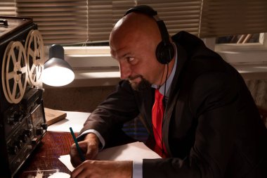 FBI 'dan ya da KGB' den gizli bir ajan kulaklıkları dinler ve konuşmayı bir makaradan makaraya kaydeder, kağıda kalemle ihbar yazar. Vatandaşların gizli telefon kayıtları..