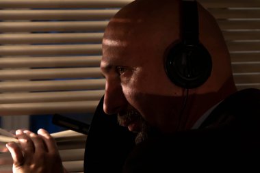 Kulaklık takan özel bir ajan jaluzilerden, seçici odak noktasından ve koyu tondan yön mikrofonuyla kulak misafiri oluyor. Konsept: istihbarat ve ajanlar, izleme ve dinleme.