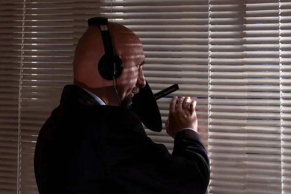 Kulaklık takan özel bir ajan jaluzilerden, seçici odak noktasından ve koyu tondan yön mikrofonuyla kulak misafiri oluyor. Konsept: istihbarat ve ajanlar, izleme ve dinleme 1.