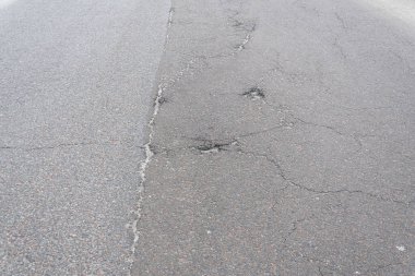 Asfalt yolda küçük çukurlar, çukurlar ve tahrip edilmiş yol yüzeyinde.
