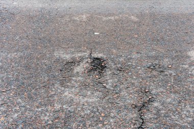 Asfalt yolda küçük çukurlar, çukurlar ve tahrip edilmiş yol yüzeyinde.