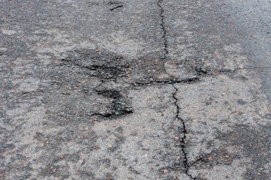 Asfalt yolda küçük çukurlar, çukurlar ve tahrip edilmiş yol yüzeyinde.