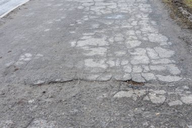 Asfalt yolda küçük çukurlar, çukurlar ve tahrip edilmiş yol yüzeyinde.