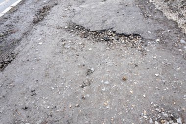 Asfalt yolda küçük çukurlar, çukurlar ve tahrip edilmiş yol yüzeyinde.