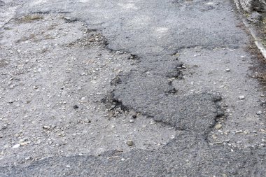 Asfalt yolda küçük çukurlar, çukurlar ve tahrip edilmiş yol yüzeyinde.