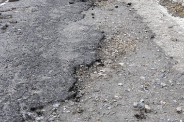 Asfalt yolda küçük çukurlar, çukurlar ve tahrip edilmiş yol yüzeyinde.