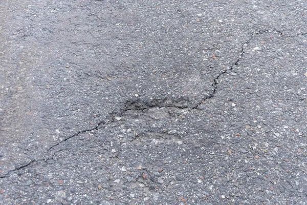Asfalt yolda küçük çukurlar, çukurlar ve tahrip edilmiş yol yüzeyinde.