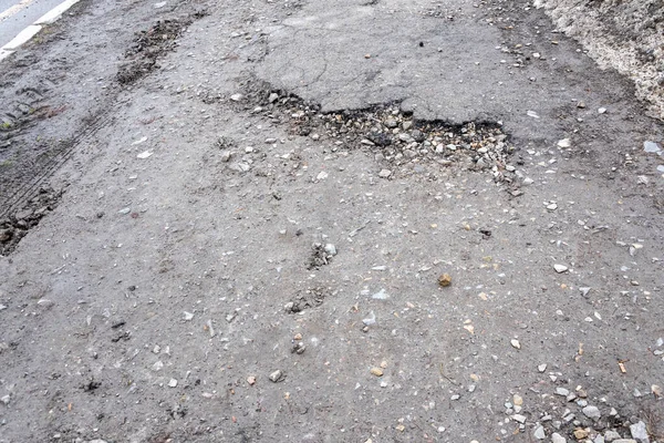 Asfalt yolda küçük çukurlar, çukurlar ve tahrip edilmiş yol yüzeyinde.