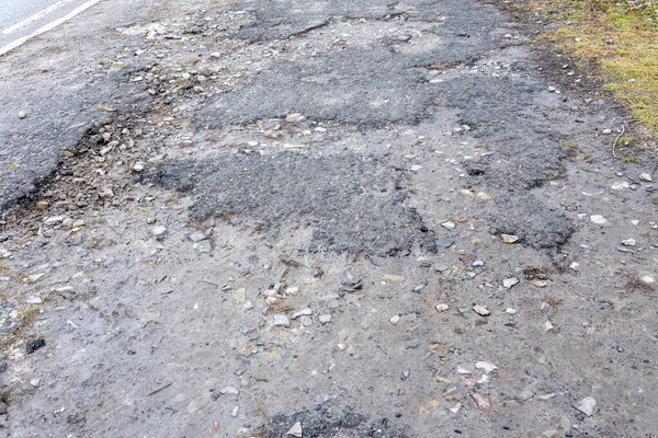 Маленькие выбоины на асфальтированной дороге, ямы и разрушенные дорожные покрытия.