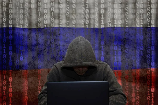 巨怪工厂 一个黑客坐在笔记本电脑前 在俄罗斯国旗的背景下 用病毒攻击和黑客攻击公司服务器 Ddos攻击 假新闻 — 图库照片