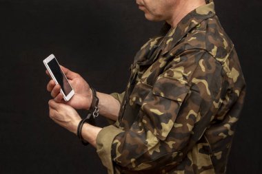 Kelepçeli bir asker karanlık bir arkaplanda, seçici bir odak noktasında telefon görüşmesi yapar. Kavram: savaş esiri telefonda konuşuyor, esir değişimi..