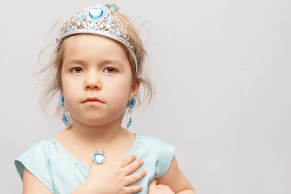 一个戴着王冠和耳环的小女孩把玩具戒指 儿童珠宝和服装珠宝展示在她的手上 — 图库照片
