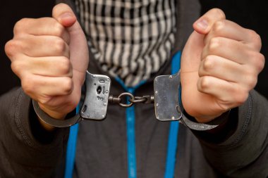 Elleri kelepçeli bir adam siyah arka planda bir mendille yüzünü gizliyor, yakın plan, seçici odaklanma. Azılı bir suçlu, cezai sorumluluk. Suç örgütü üyeleri ve çeteler.