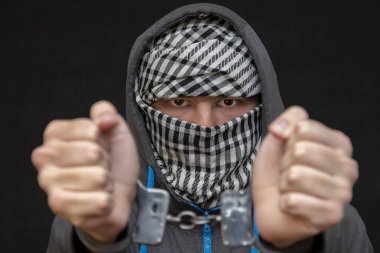 Elleri kelepçeli bir adam siyah arka planda bir mendille yüzünü gizliyor, yakın plan, seçici odaklanma. Azılı bir suçlu, cezai sorumluluk. Suç örgütü üyeleri ve çeteler.