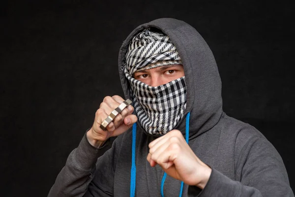 暗い背景に顔を覆うスカーフを持つ男の手に真鍮ナックル 選択的な焦点 フーリガンのストリートファイト 市民への攻撃 都市犯罪 — ストック写真