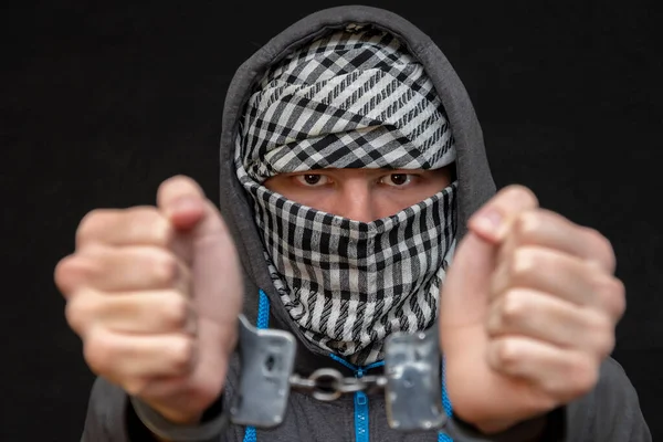 Elleri kelepçeli bir adam siyah arka planda bir mendille yüzünü gizliyor, yakın plan, seçici odaklanma. Azılı bir suçlu, cezai sorumluluk. Suç örgütü üyeleri ve çeteler.