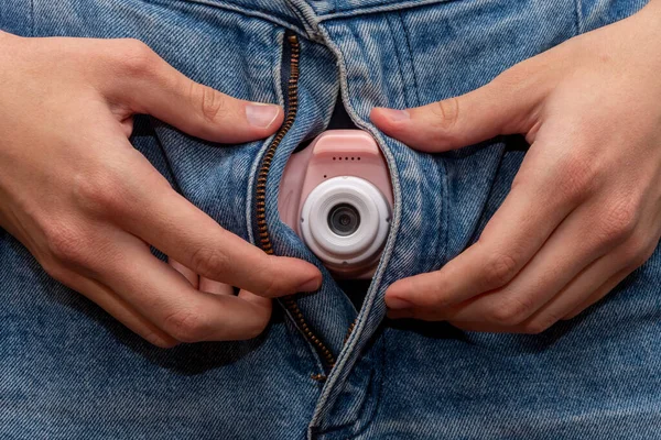 A man holds a spy camera in the fly of his denim pants. Concept: collecting compromising material, a bed scene, a sexy man.