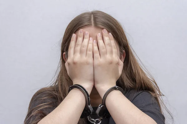 一个被戴上手铐的年轻女孩把脸隐藏在灰蒙蒙的背景下 身穿黑色T恤的少年犯 未成年人的刑事责任 — 图库照片