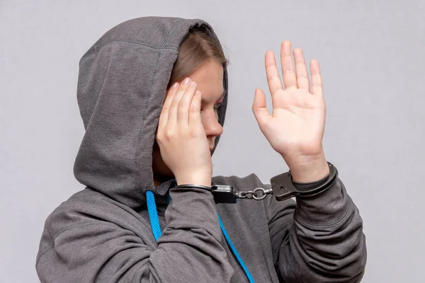 一个十几岁的女孩被戴上手铐 藏在一个灰色背景的帽衫里 少年犯 未成年人的刑事责任 青年犯罪集团和帮派成员 — 图库照片