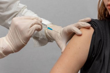 Doktor aşıyı arka planda, yakın planda bir kızın omzuna enjekte ediyor..