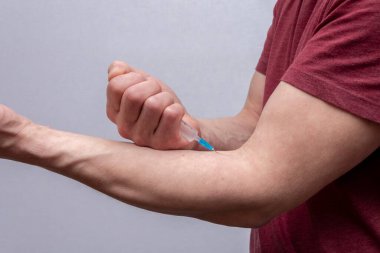 Yaşlı, kaslı bir adam kolundaki damara iğne yapıyor. Yakın plan. Belki de ağrı kesici enjekte ediyordur. Yaşlı bir uyuşturucu bağımlısı bir doz enjekte ediyordur..