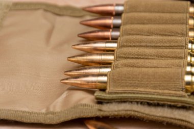 Tahta arka planda 7.62 kalibrelik bir askeri bandocuda kurşun bulunan sarı muharebe tüfeği fişekleri..