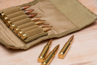 Tahta arka planda 7.62 kalibrelik bir askeri bandocuda kurşun bulunan sarı muharebe tüfeği fişekleri..