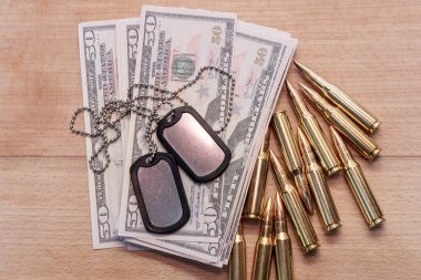 Amerikan dolarlarının arka planına karşı, gerçek cephane ve ordu kimlik madalyonları. Konsept: Askeri özel operasyon, silah tedariği, savaşın finansmanı.