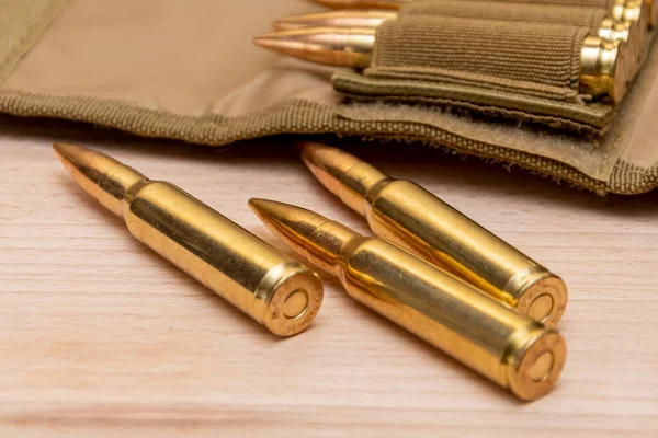 Tahta arka planda 7.62 kalibrelik bir askeri bandocuda kurşun bulunan sarı muharebe tüfeği fişekleri..