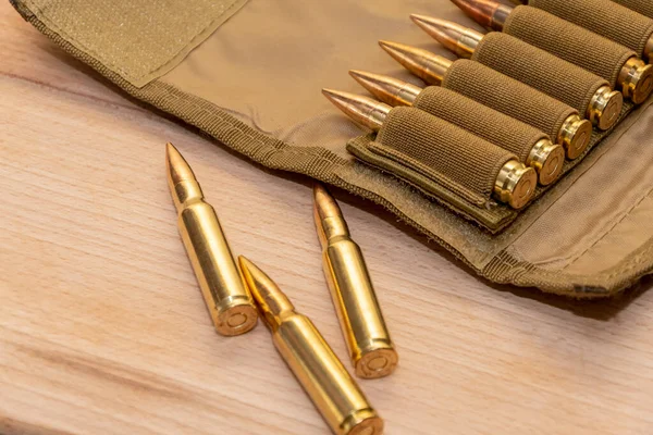 Tahta arka planda 7.62 kalibrelik bir askeri bandocuda kurşun bulunan sarı muharebe tüfeği fişekleri..