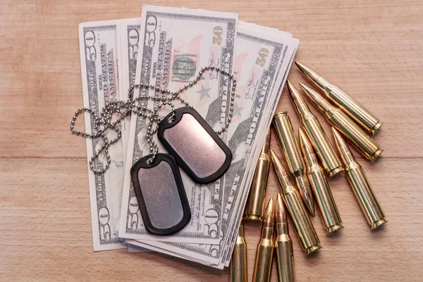 Amerikan dolarlarının arka planına karşı, gerçek cephane ve ordu kimlik madalyonları. Konsept: Askeri özel operasyon, silah tedariği, savaşın finansmanı.