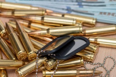 Amerikan dolarlarının arka planına karşı, gerçek cephane ve ordu kimlik madalyonları. Konsept: Askeri özel operasyon, silah tedariği, savaşın finansmanı.