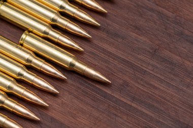 Kalaşnikof saldırı tüfeğinden çıkan gerçek mühimmat ve fişekler tahta arka planda bir sırada yatıyor. Merkezde bir fişek ileri itilir. Konsept: ileri hareket, saldırı.