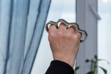 Blow with brass knuckles. The hand of an elderly woman clutches a metal brass knuckles. Concept, women's self-defense, traumatic objects, family quarrel, domestic scandal, domestic crime and violence.