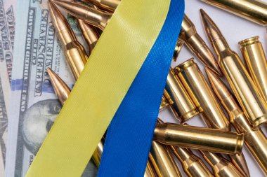 Ribbons of the Ukrainian flag, cartridges and 100-dollar bills, close-up, selective focusing. Concept: sale of weapons under lend-lease, assistance with weapons, the war in Ukraine, trade in ammunition.