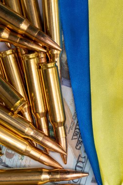 Ukrayna bayrağı şeritleri, kartuşlar ve 100 dolarlık banknotlar, yakın plan, seçici odaklanma. Konsept: ödünç verilen silahların satışı, silahlara yardım, Ukrayna 'daki savaş, cephane ticareti.