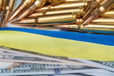 Ribbons of the Ukrainian flag, cartridges and 100-dollar bills, close-up, selective focusing. Concept: sale of weapons under lend-lease, assistance with weapons, the war in Ukraine, trade in ammunition.