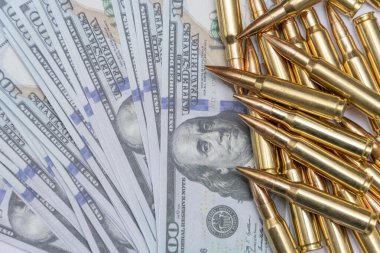 Scattered cartridges with bullets on 100 dollar bills, close-up, selective focusing. Concept: sale of weapons under lend-lease, assistance with weapons, mercenary in the army, trade in ammunition.