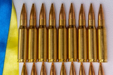 Ukrayna bayrağı şeritleri ve Kalaşnikof saldırı tüfeği için 7.62 kalibrelik fişekler, seçici odaklanma. Konsept: Ukrayna 'da kiralık silahların tedarik edilmesinde yardım,